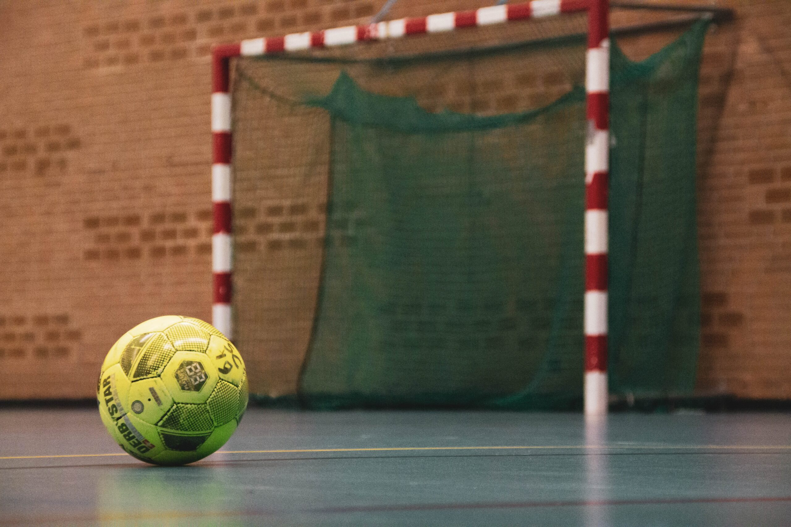 En gul fotboll ligger på golvet framför ett mål